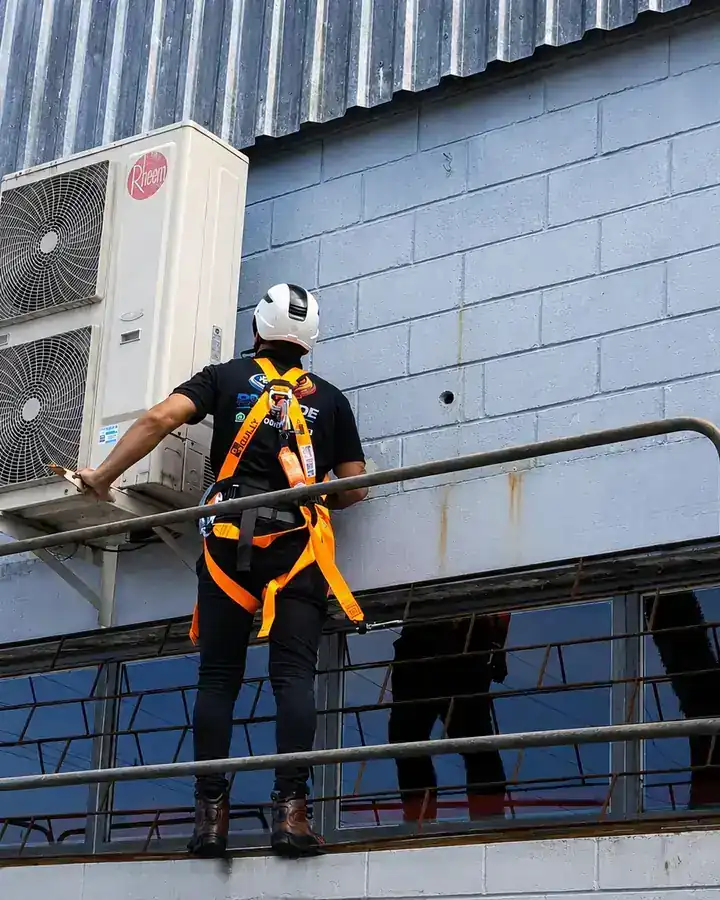 Técnico da Progride com cinto de segurança e capacete atendendo condensadora em altura